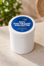 Load image into Gallery viewer, White 1 kg Adize64 raw organic shea butter jar with a blue lid label on a stone surface with greenery behind it.
